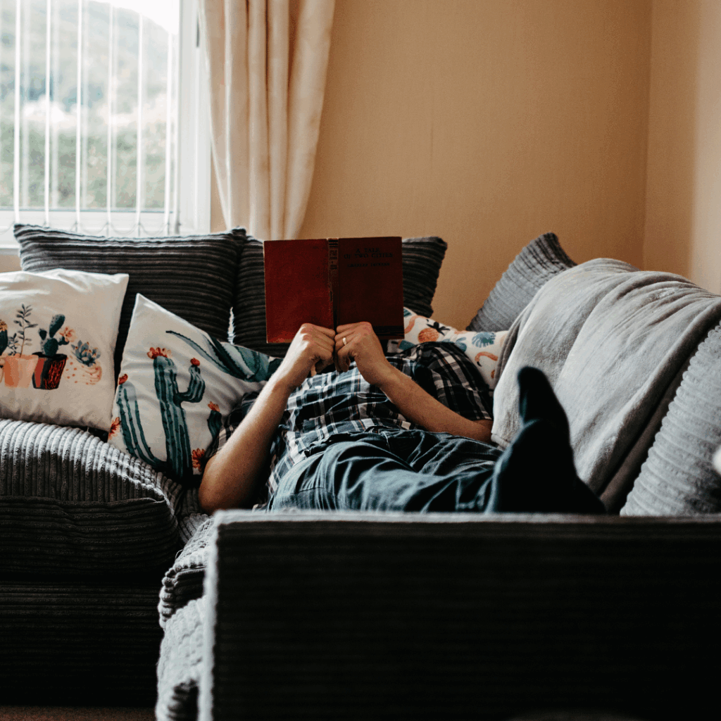 Man laying on couch and reading his book.